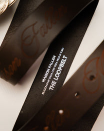 Close-up of a black belt with 'Maison Fallen' branding on a white background